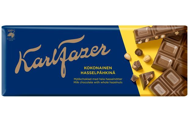 A blue and yellow Fazer wrapper with bold gold script shows "Fazer Milk Chocolate Whole Hazelnuts," featuring chocolate pieces and whole hazelnuts beside the bar.