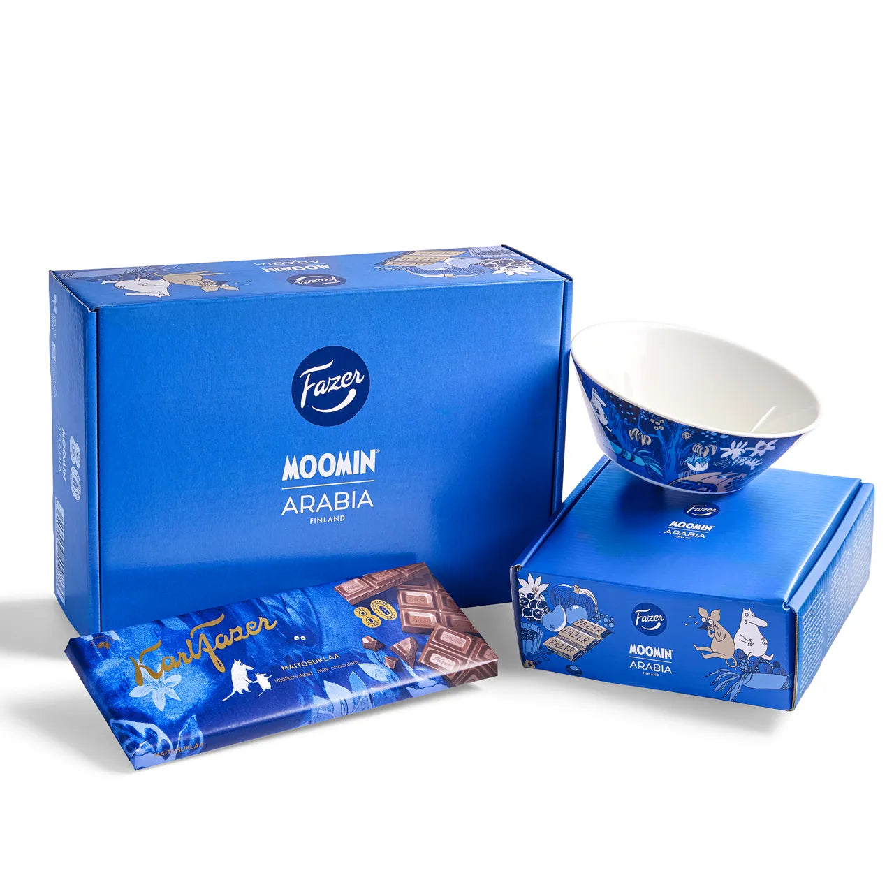 The Fazer x Moomin 80 Year Anniversary Box set features a Fazer Milk Chocolate bar, an Arabia celebration bowl with Moomin characters, and two blue anniversary boxes with Finland branding and delightful Moomin illustrations.