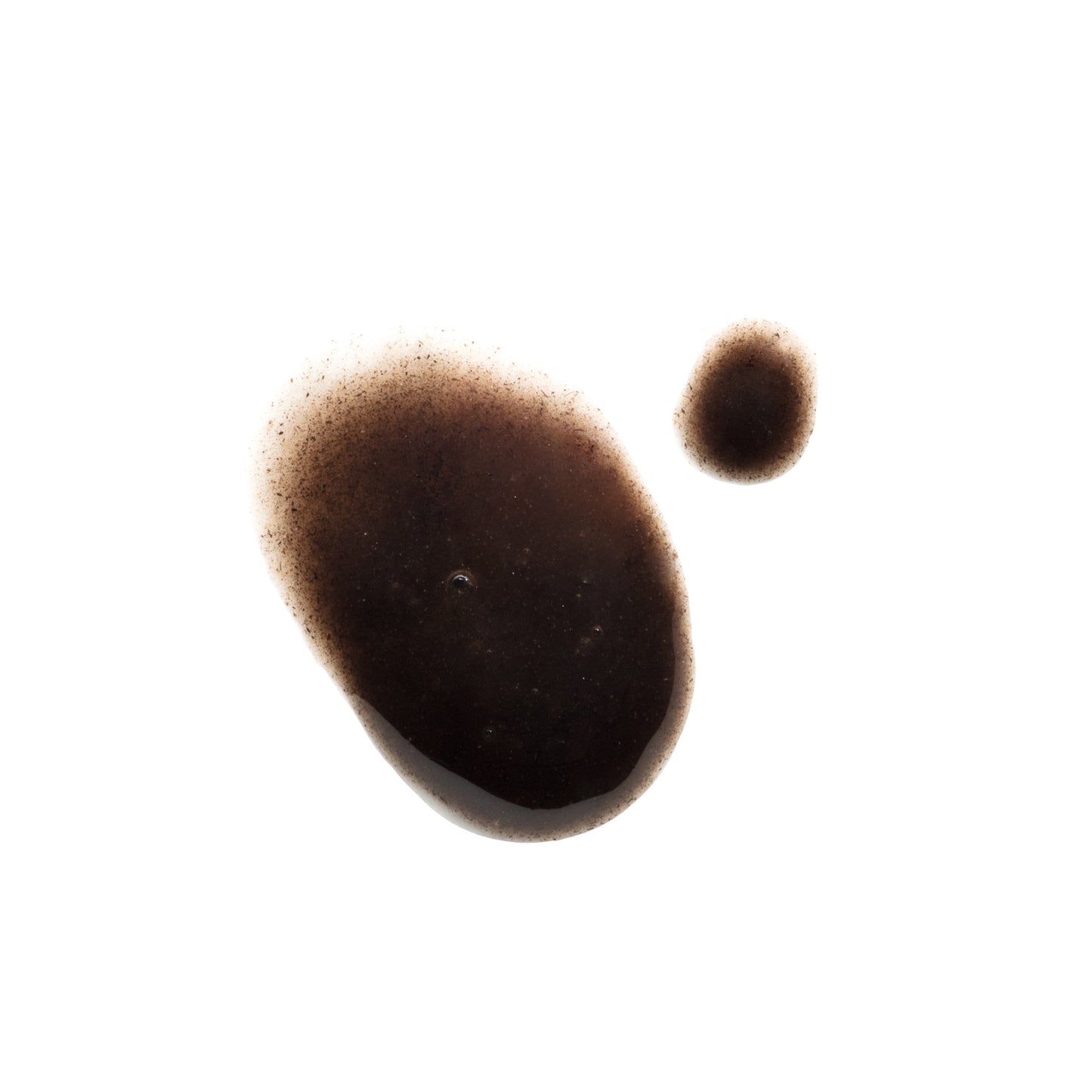 Two irregular brown liquid drops, one large and one small, sit on a white background with slightly fuzzy edges. The glossy semi-transparent look suggests NOBE Forest DropsĀ® Microbiome Booster by NOBE Nordic Beauty.