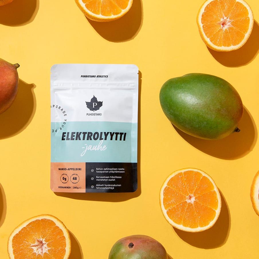 A packet of Puhdistamo Electrolyte Powder Mango & Orange sits on a yellow surface with halved oranges, whole tangerines, and mangoes—ideal for ketogenic diets. The Puhdistamo packaging displays blue, white, and orange colors.