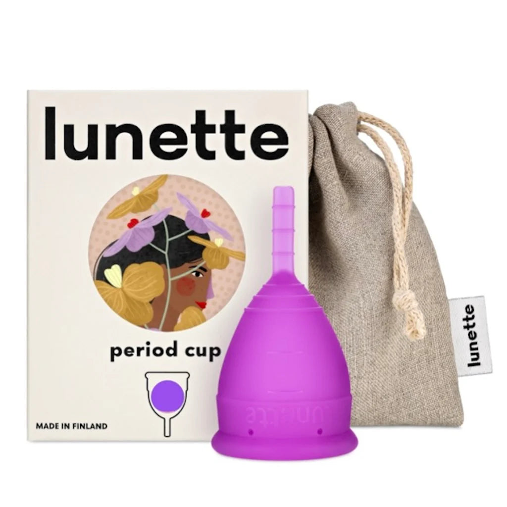 A purple Lunette Menstrual Cup by Lunette sits next to its box, which features a woman with flowers in her hair. An eco-friendly period solution, it comes with a drawstring pouch for storage.