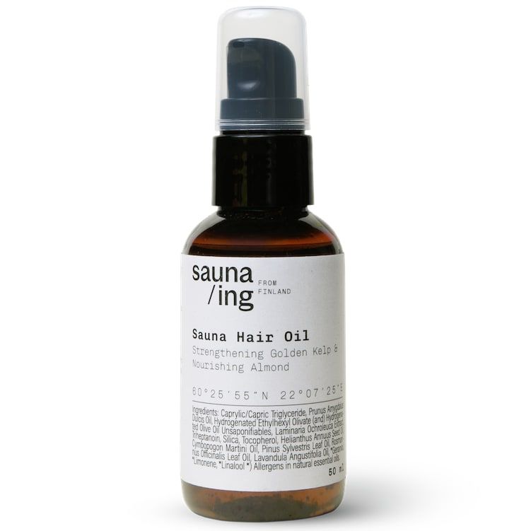 A brown bottle of sauna/ing Sauna Hair Oil with a black pump and white label, featuring Strengthening Golden Kelp & Nourishing Almond for heat protection and frizz control. The label lists ingredients, location coordinates, and the sauna/ing brand.