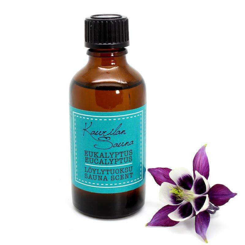 A brown glass bottle of Kaurilan Sauna Eucalyptus Sauna Scent by Kaurilan Sauna, with a blue label, stands next to a purple and white flower on a white background—ideal for fragrant sauna experiences.