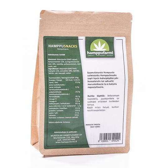 A brown paper package of Nordic Hempfarm HempSnacks stands upright, showing a green and white label with Finnish product details, nutritional facts, and usage instructions for these lightly salted snacks.