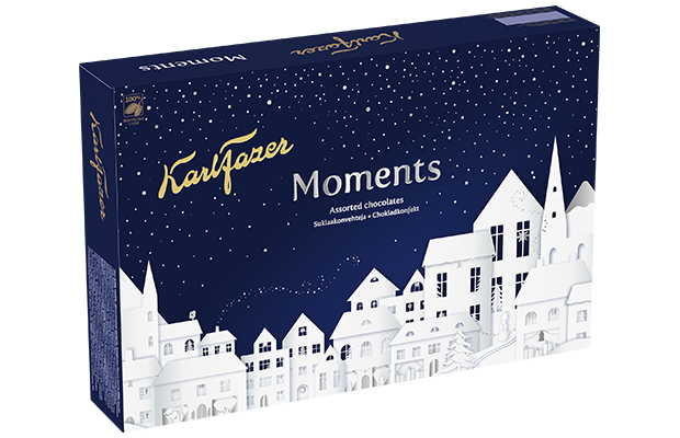 Die Fazer Moments Assorted Chocolates von Fazer kommen in einer dunkelblauen Schachtel mit goldener Schrift und einer weißen, verschneiten Stadtillustration in sternenklarer Nacht, die den Zauber finnischer Schokolade einfängt.