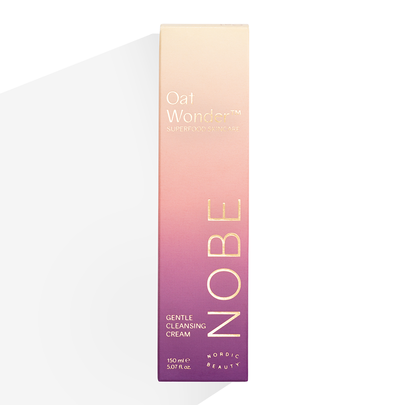 Eine rechteckige Schachtel mit der Oat Wonder® Gentle Cleansing Cream von NOBE Nordic Beauty, einem cremigen Gesichtsreiniger mit Fazer-Haferöl, zeigt einen rosa und violetten Farbverlauf und goldenen Text, aufrecht stehend vor einem weißen Hintergrund.