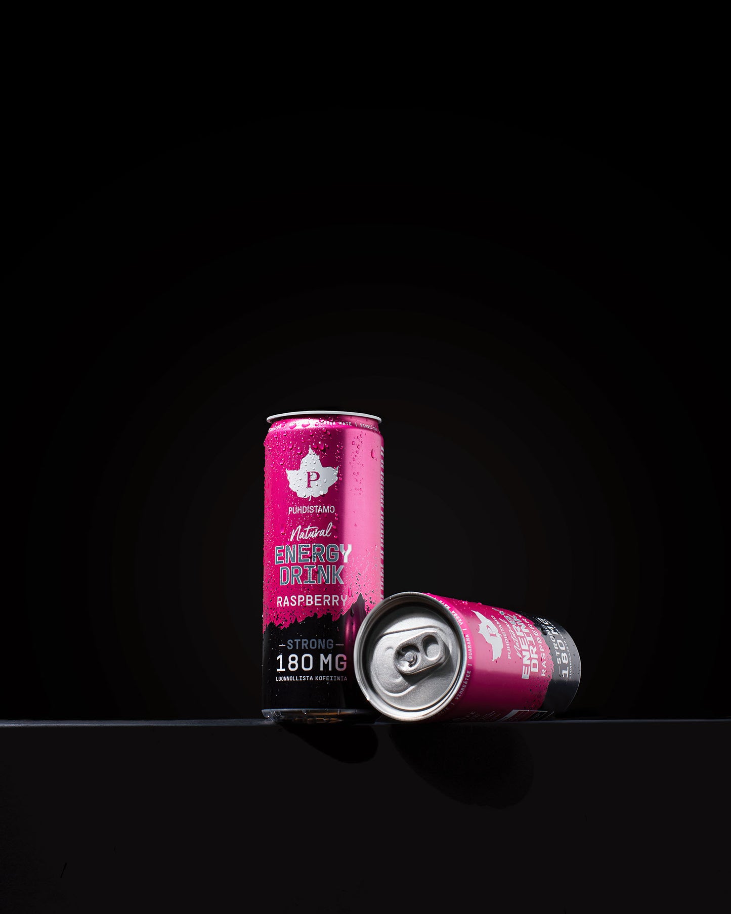 Zwei Dosen Puhdistamo Natural Energy Drink Raspberry Strong sind vor einem schwarzen Hintergrund abgebildet; eine steht aufrecht mit Kondenswasser, während die andere teilweise geöffnet ist und auf der Seite vor ihr liegt.