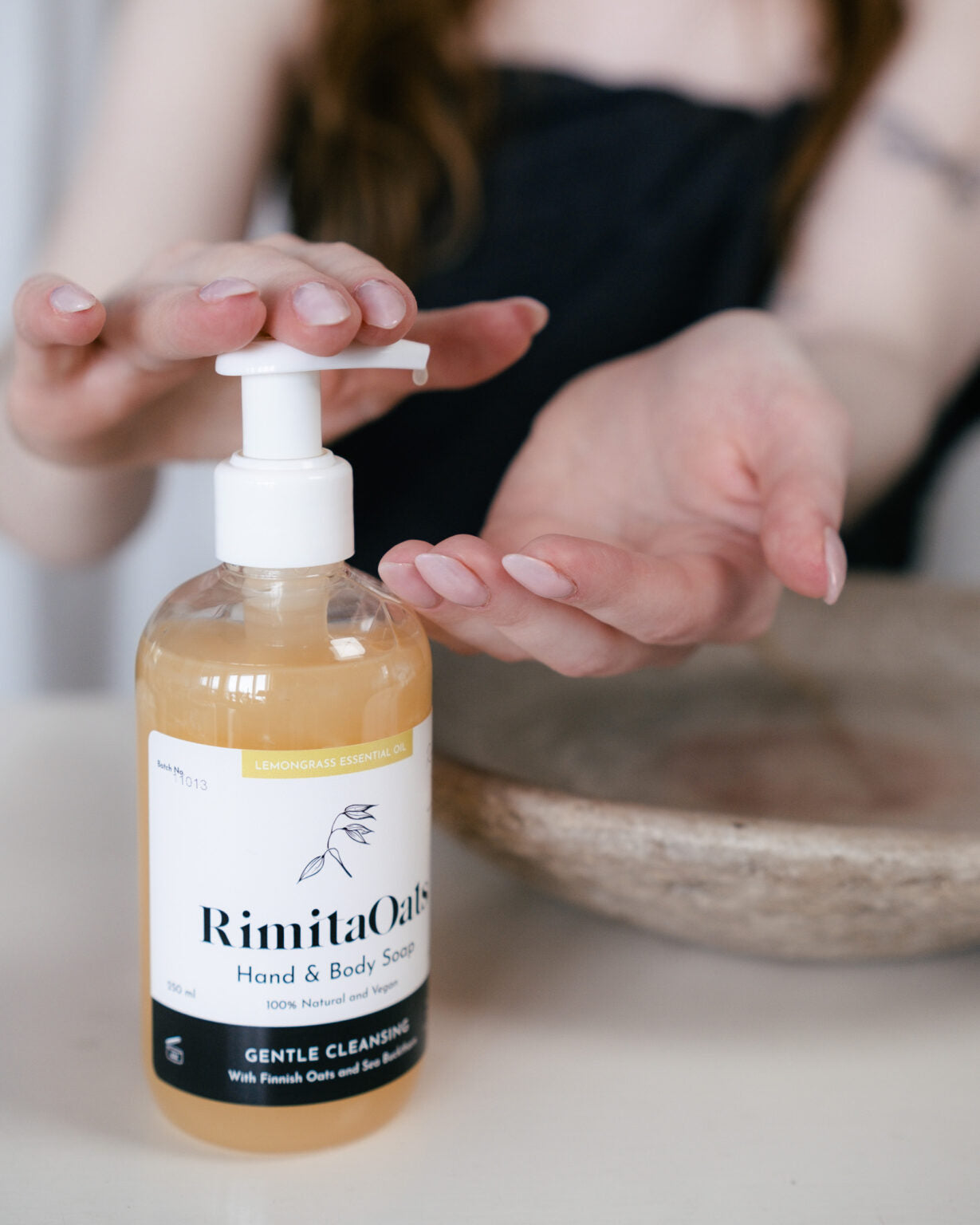 Eine Person drückt eine Pumpflasche mit der RimitaOats Hand- und Körperseife von Rimita Green und gibt die Seife auf ihre offene Handfläche ab. Das Bild konzentriert sich auf die sanfte Pflege empfindlicher Haut mit finnischem Hafer, wobei die Flasche und die Hände im Mittelpunkt stehen und der Hintergrund verschwommen ist.