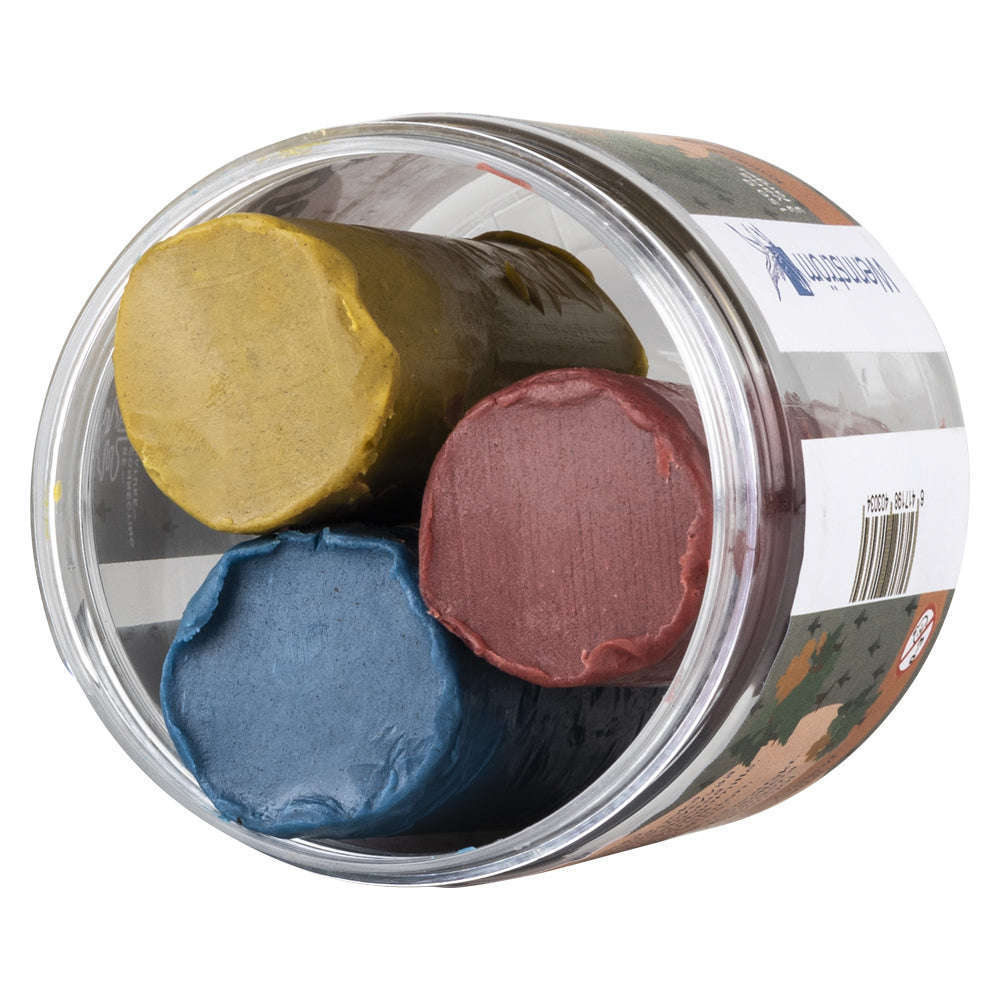 Ein durchsichtiger, runder Behälter von Wennström enthält drei nebeneinander angeordnete Forest Plasticine Gesichtsmalstifte in braunen, grün-gelben und blauen Farbtönen.