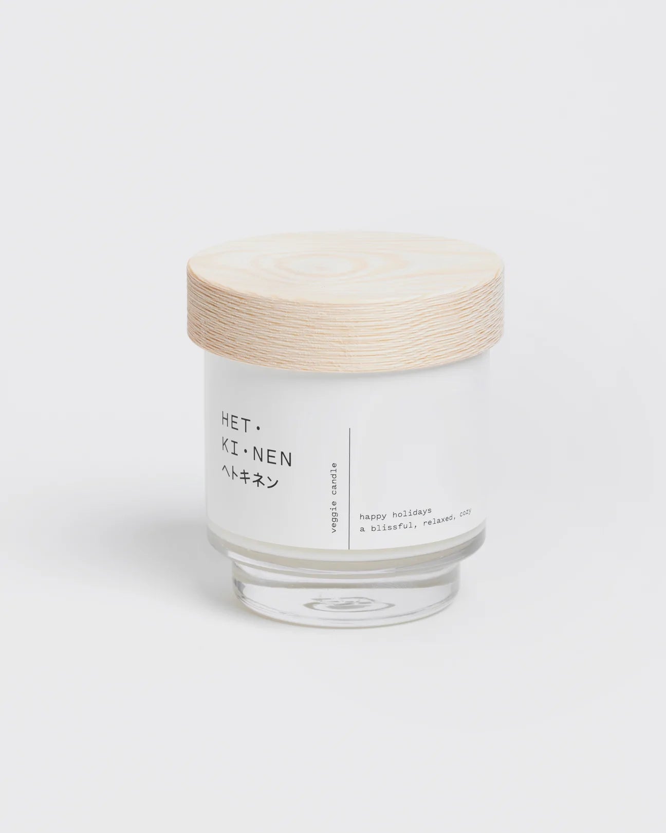 Die Veggie Candle Happy Holidays von Hetkinen ist eine minimalistische Kerze im Glas mit einem Deckel aus hellem Holz, einem Docht aus Espenholz und einem Etikett mit japanischem Akzent - perfekt für gemütliche, glückliche Winternächte.