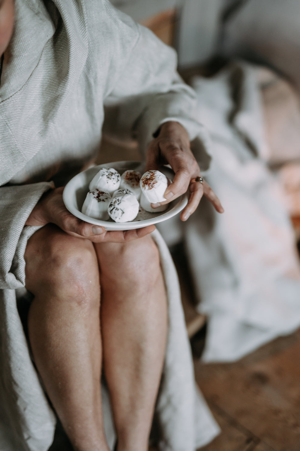 Eine Person in einem hellen Bademantel sitzt im Schneidersitz und hält das Kaurilan Sauna Peppermint Footbath von Kaurilan Sauna. Das handgefertigte Produkt hebt sich von einem sanft verschwommenen, gemütlichen neutralen Hintergrund ab.