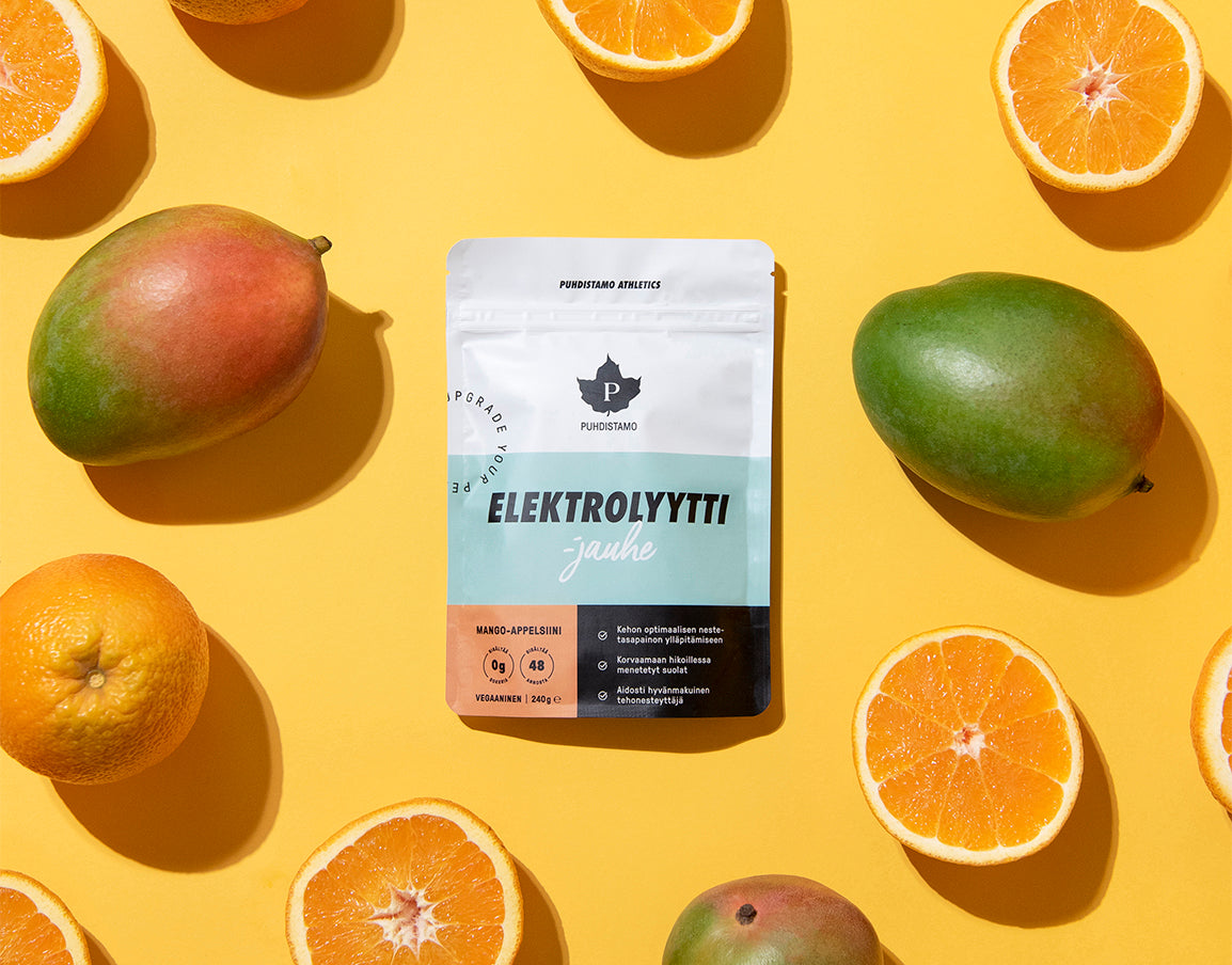 Eine Packung Puhdistamo Elektrolytpulver Mango & Orange liegt auf einer gelben Fläche mit halbierten Orangen, ganzen Mandarinen und Mangos - ideal für ketogene Diäten. Die Puhdistamo-Verpackung ist in den Farben Blau, Weiß und Orange gehalten.