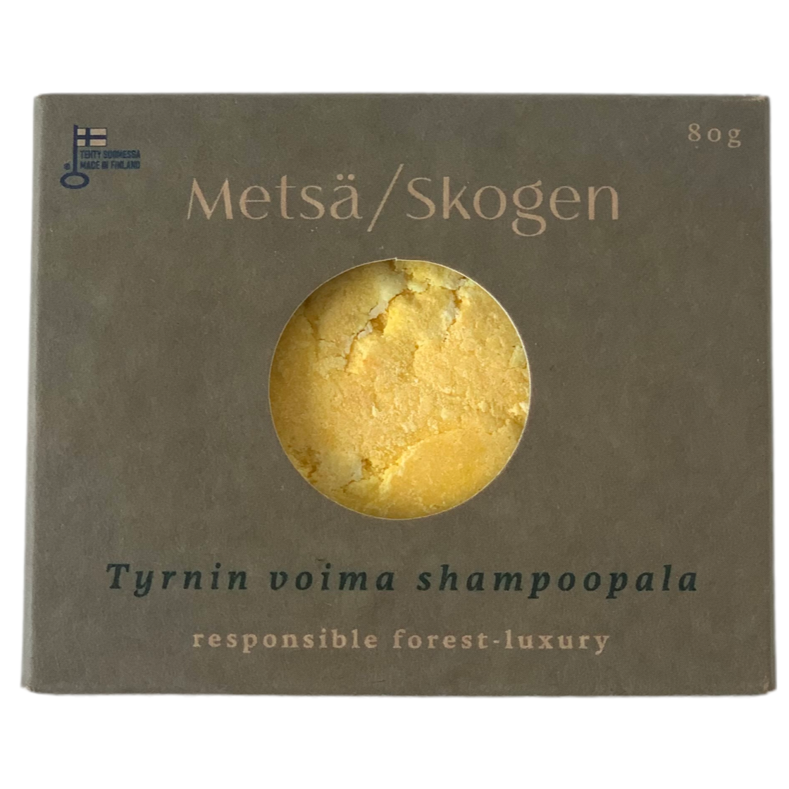 Metsä/Skogen The Power of Sanddorn Shampoo Bar, handgefertigt in Finnland. Die graue Schachtel hat ein rundes Fenster, das den gelben 80g-Riegel zeigt, mit goldener und weißer Schrift. Inklusive Etiketten in Finnisch und Englisch.