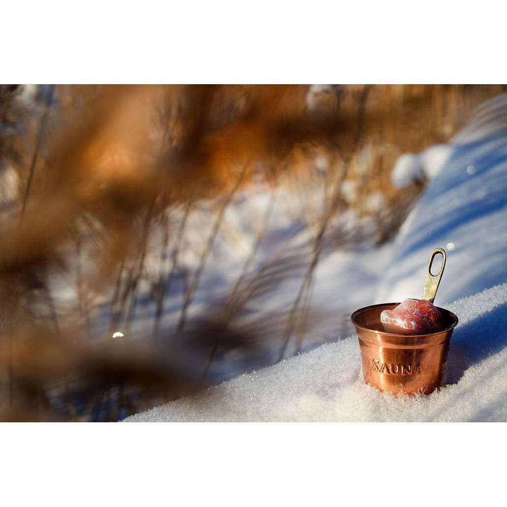 Der Emendo Stove Cup & Himalaya Salt ruht auf verschneitem Boden im Freien und hält ein Stück Eis. Im Hintergrund deutet unscharfes trockenes Gras auf die erfrischende Allergielinderung durch Saunadampf mit dem Qualitätsprodukt von Emendo hin.