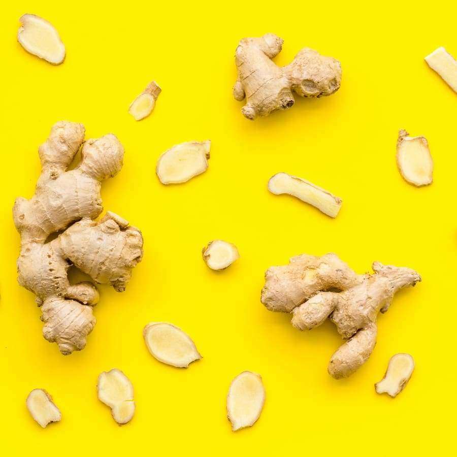 Ganze Ingwerwurzeln und -scheiben sind auf einem leuchtend gelben Hintergrund verstreut und erinnern an die Inhaltsstoffe von Havuka Cabbage-Ginger-Spruce Resin Balm by Havuka zur natürlichen Linderung von Arthrose-Schmerzen.