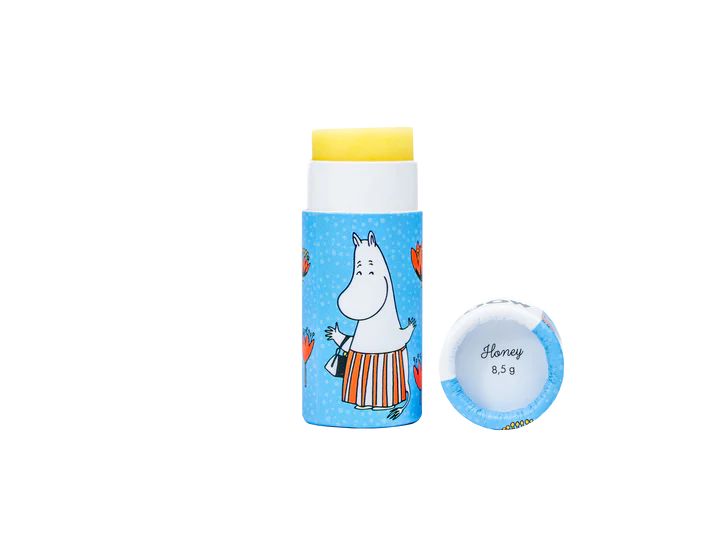 Un tube de baume à lèvres Gustaf & Linnea Moomin Moominmamma avec un emballage bleu, des cœurs orange et un personnage Moomin dessiné. Le bouchon est retiré, révélant l'étiquette Honey 8,5 g à l'intérieur. Produit écologique de Gustaf & Linnea.