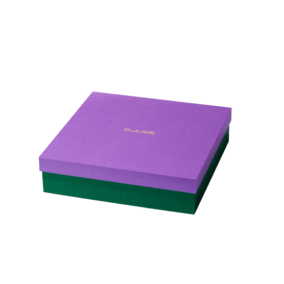 Une boßte carrée verte avec un couvercle violet et le texte DJUSIE en lettres dorées sur le dessus met en valeur le coffret de soins pour la peau Djusie Full Bloom Box de Djusie, idéal pour ranger les produits de soins pour la peau. La boßte est présentée sur un fond blanc uni.