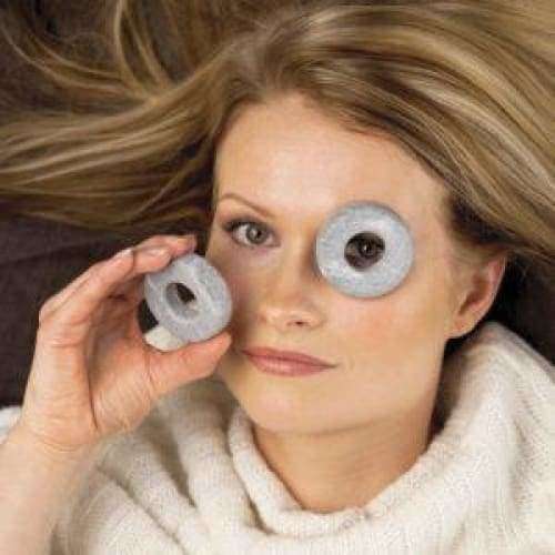 Une femme aux longs cheveux blonds et à l'expression calme porte un pull blanc et tient de manière ludique des pierres Hukka Orbits Eye Stones de Hukka sur ses yeux, comme s'il s'agissait de lunettes.