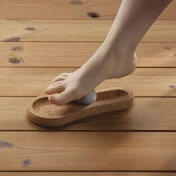 Une personne utilise le Hukka Solejoy en massant la plante de son pied nu sur sa pierre ronde, fixée dans une base en bois en forme de pied de Hukka.