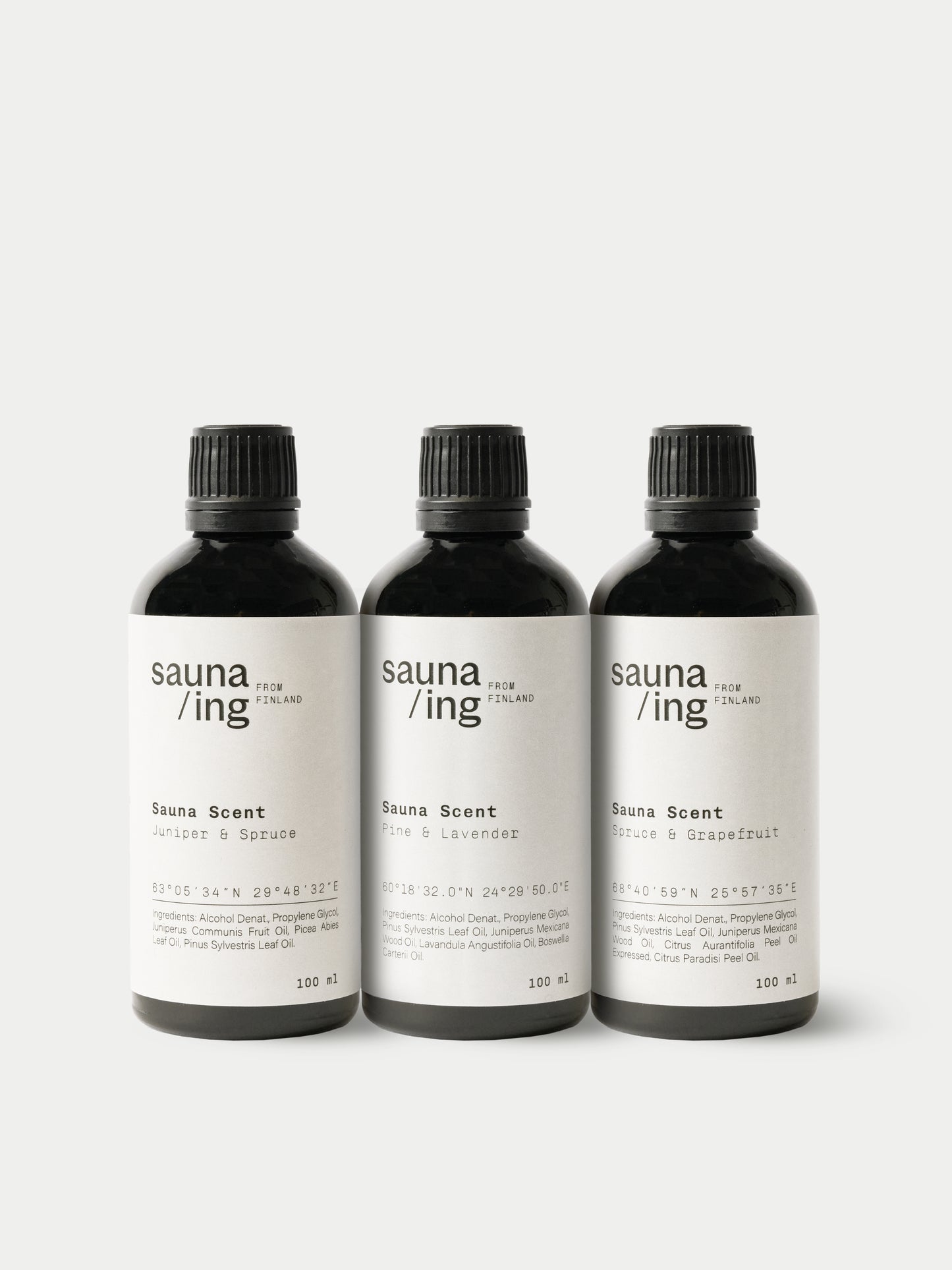 Tre bottiglie nere di sauna/ing Sauna Scent Juniper & Spruce di sauna/ing sono disposte una accanto all'altra su uno sfondo bianco. Ogni bottiglia contiene fragranze uniche, come abete rosso e ginepro, per un'autentica esperienza di sauna finlandese.