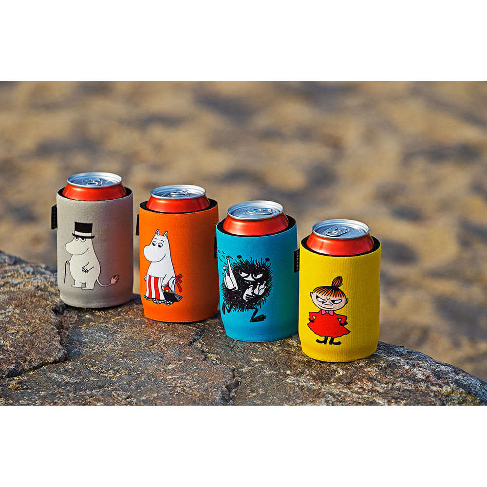 Quattro lattine di soda nelle custodie in neoprene Emendo Moomin Cooler Moominmamma - grigia, arancione, blu e gialla - sono appoggiate su una roccia all'aperto, con i personaggi Moomin visibili su uno sfondo sabbioso sfocato.