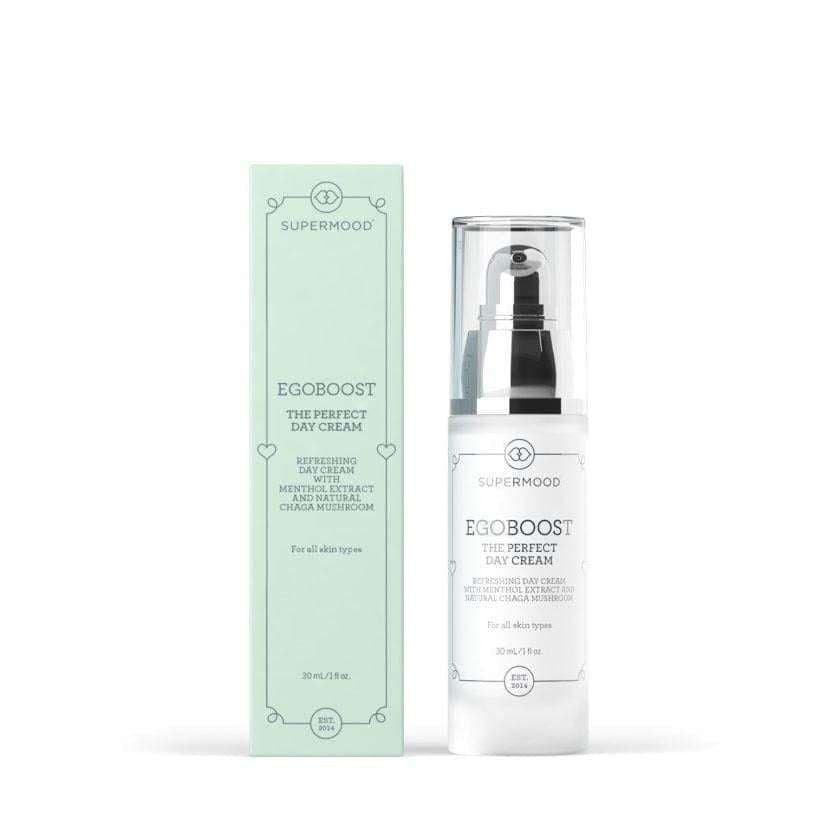 Een fles Supermood Egoboost The Perfect Day Cream staat naast de lichtgroene doos, beide met een minimalistisch ontwerp en tekst waarin staat dat de moisturizer geschikt is voor alle huidtypes en Finse Chaga-paddenstoelenextract bevat.