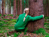 A woman in a green sweater hugging a tree in a forest