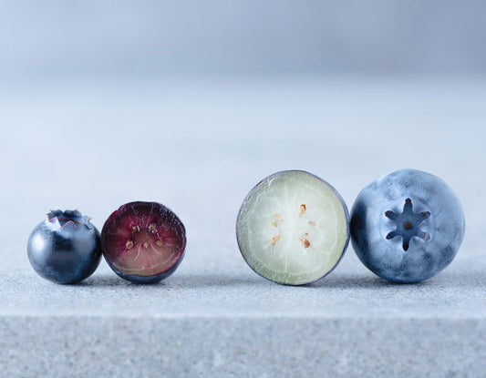 Halved bilberry with purple flesh next to a halved blueberry with pale flesh