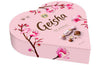 The Fazer Geisha Gift Box is a heart-shaped pink box of Finnish chocolate, decorated with cherry blossom art, the Geisha logo, and images of milk chocolate with hazelnut filling by Fazer.