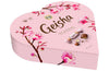 The Fazer Geisha Gift Box is a heart-shaped pink box of Finnish chocolate, decorated with cherry blossom art, the Geisha logo, and images of milk chocolate with hazelnut filling by Fazer.