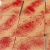 A close-up of rectangular beige tiles or boards with a red speckled pattern across the surface, arranged in a grid.