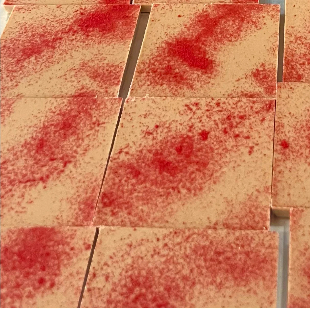 A close-up of rectangular beige tiles or boards with a red speckled pattern across the surface, arranged in a grid.