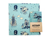 The Gustaf & Linnea Moomin Beeswax Food Wrap features navy Moomin characters skiing, skating, and near a tower on a light blue background with white snowflakes—an eco-friendly, reusable, and charming food storage solution.