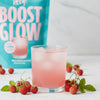 Glass of pink drink with strawberries and a 'Boost Glow' product in the background