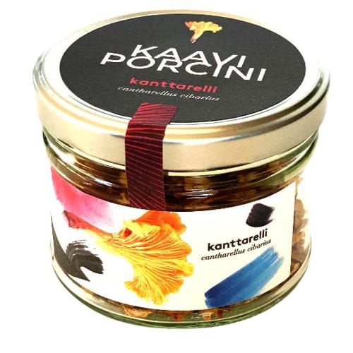 Kaavi Porcini Dried Chanterelle comes in a glass jar with a silver lid, featuring a colorful label with brush strokes and a yellow mushroom illustration. Enjoy premium Finnish dried chanterelles from Kaavi Porcini.