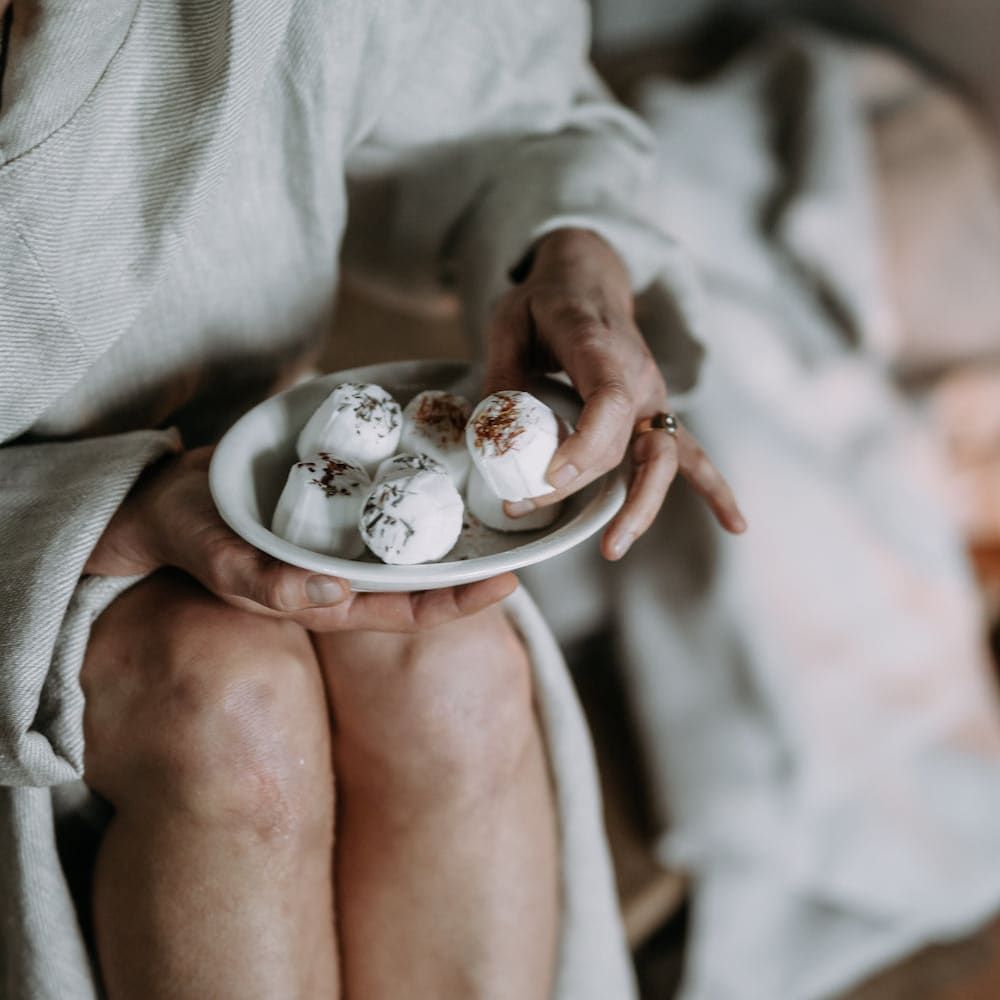 A person in a light robe holds a Kaurilan Sauna Lemongrass Footbath from Kaurilan Sauna in their lap, focusing on their hands gently cradling the soothing product.