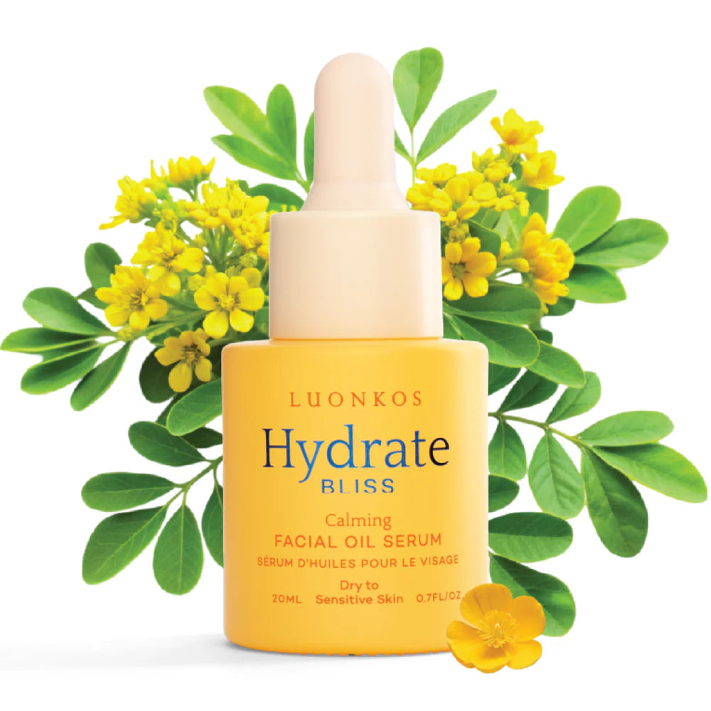 A yellow dropper bottle labeled Luonkos Bliss Facial Oil Serum sits before green branches with small yellow flowers. This fragrance-free serum by Luonkos is specially formulated for dry and sensitive skin.