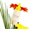 A bottle of Luonkos Precious Intimate Oil, ideal for sensitive skin and dryness, rests among green palm leaves and bright orange and yellow flowers on a white background.