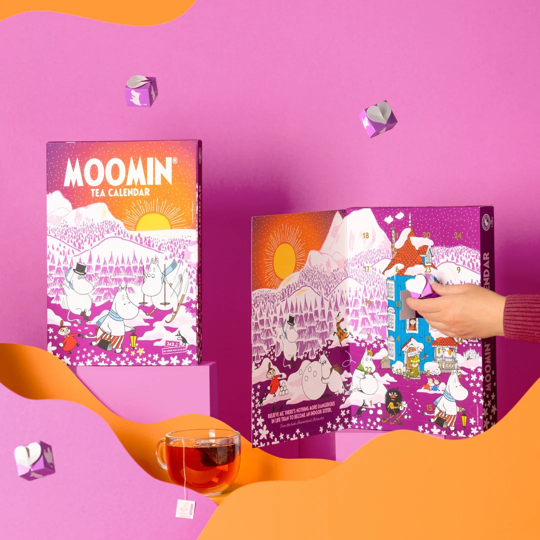 Moomin Tea Calendar set displayed on a bright pink background with orange abstract shapes. One calendar is closed, showing the illustrated cover, and another is open with a hand sliding a door to reveal a small Moomy house.
