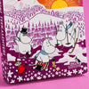 A Moomin-themed Advent calendar box featuring Moomy characters in a winter mountain scene, photographed against a solid pink background.