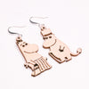 Coruu Moomin Wooden Earrings by Coruu feature charming cartoon hippos—one with a skirt and necklace, the other with a top hat and cane—crafted from wood with black line details and finished with metal hooks for easy Nordic-inspired styling.
