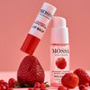 The Mossa Berry Kiss Gift Set featuring hydrating lip balm and overnight peeling serum is displayed among strawberries, raspberries, and lingonberries against a pink background.