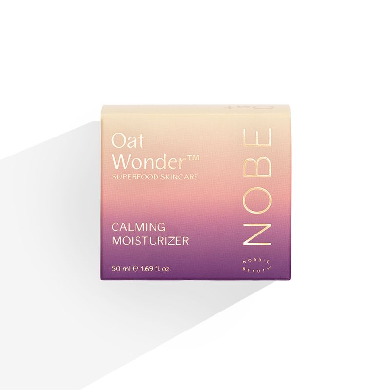 A box of NOBE Oat Wonder® Calming Moisturizer, 50 ml by NOBE Nordic Beauty—a vegan moisturizer with Fazer Oat Oil for sensitive skin. The beige and purple gradient packaging displays product details in white and gold.