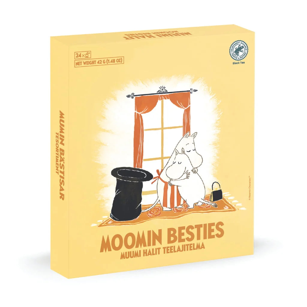 A yellow Moomin Besties tea box featuring an illustration of Moomin characters in front of a window with orange curtains, a black top hat, and a striped rug. The box is shown at a three-quarter angle on a white background.