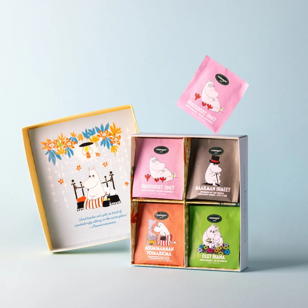 A Moomin-themed tea gift set with an illustrated outer box, a floating pink tea packet, and a smaller open box showing four colorful tea bags: Pink Mammoth Mint, Gray Mammoth Juice, Orange Vohadoka, and Green Colet Mäki.