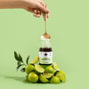 A hand holds a golden spoon with Puhdistamo Daily Electrolyte Powder Lime above a jar, surrounded by fresh whole and sliced limes, set against a light green background. The product is from the brand Puhdistamo.