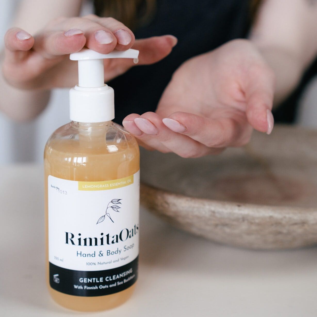 A person presses a pump bottle of Rimita Green’s RimitaOats Hand and Body Soap, dispensing soap onto their open palm. The image focuses on gentle care for sensitive skin with Finnish oats, with the bottle and hands in focus and a blurred background.