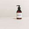 A brown pump bottle of SEES Company’s SEES Hand & Body Lotion with organic birch sap rests on a light surface against an off-white background.