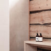 A minimalist interior with a light wooden bench displays two SEES Company Shampoo No. 1 Cedar & Orange bottles against a rustic wood wall. Soft natural lighting and earthy tones evoke a serene vegan haircare ritual.