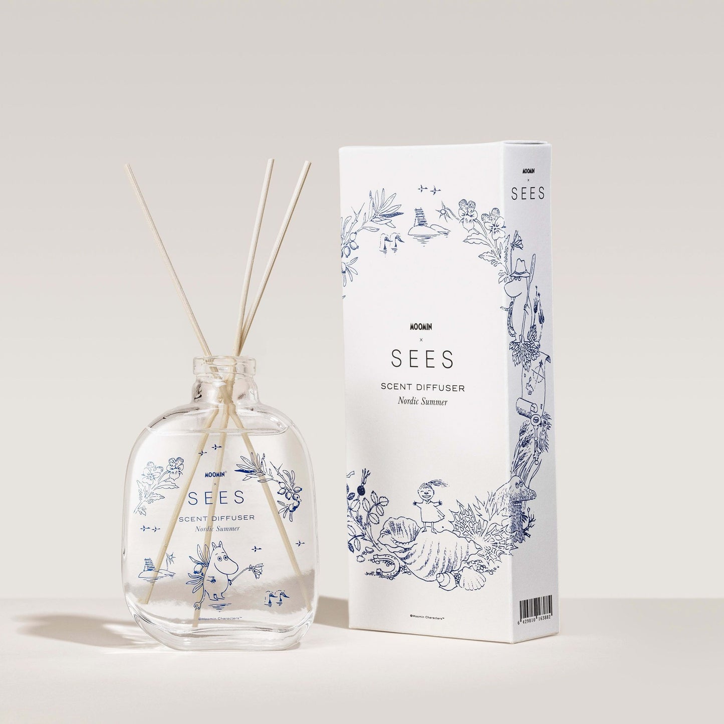The SEES Company SEES x Moomin Room Diffuser Nordic Summer, in a clear glass bottle with wooden sticks and a white box adorned with blue floral graphics, captures the fresh essence of a Nordic summer against a neutral backdrop.